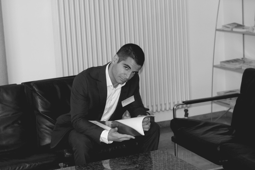schwarz-weiß Bild von einem jungen Mann im Anzug, der im sitzen in einem Heft blättert